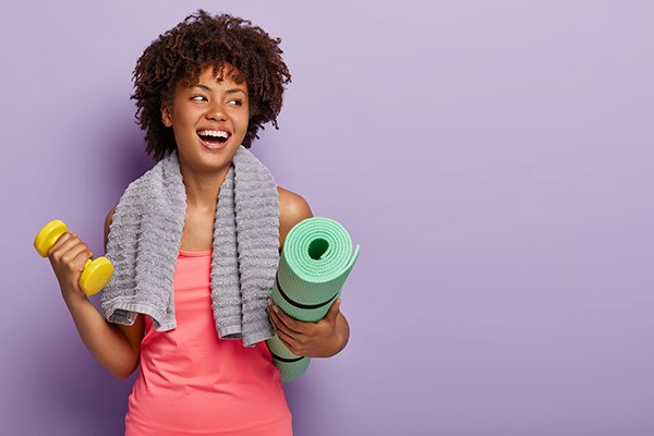 Positive Dark Skinned Woman Holds Yoga Mat And Dumbbell, Wears S exercise happiness